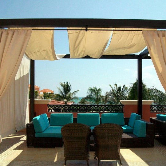 Outdoor seating area with turquoise sofas, brown chairs, and beige curtains on a sunny day.
