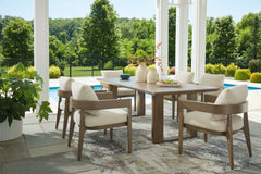Outdoor dining set with wooden table and chairs on a patio with pool and garden view.